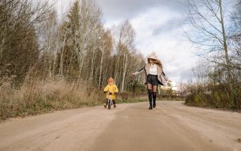 Woman and child on a dirt road in autumn forest, enjoying outdoor fun and nature.